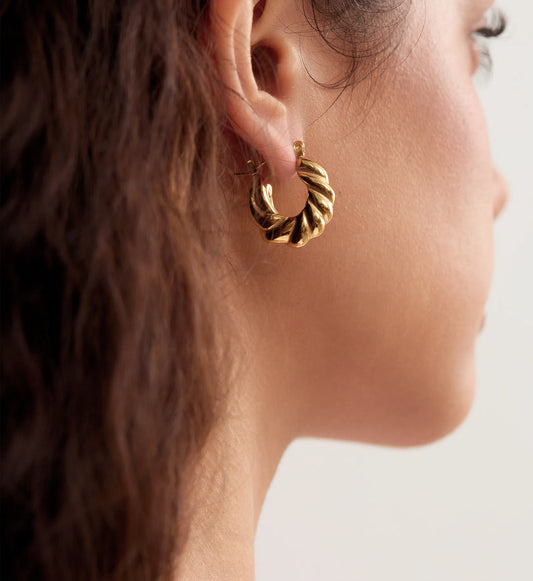 Close-up image of gold stainless steel Twisted Hoop Earrings on a model by Liora Senar