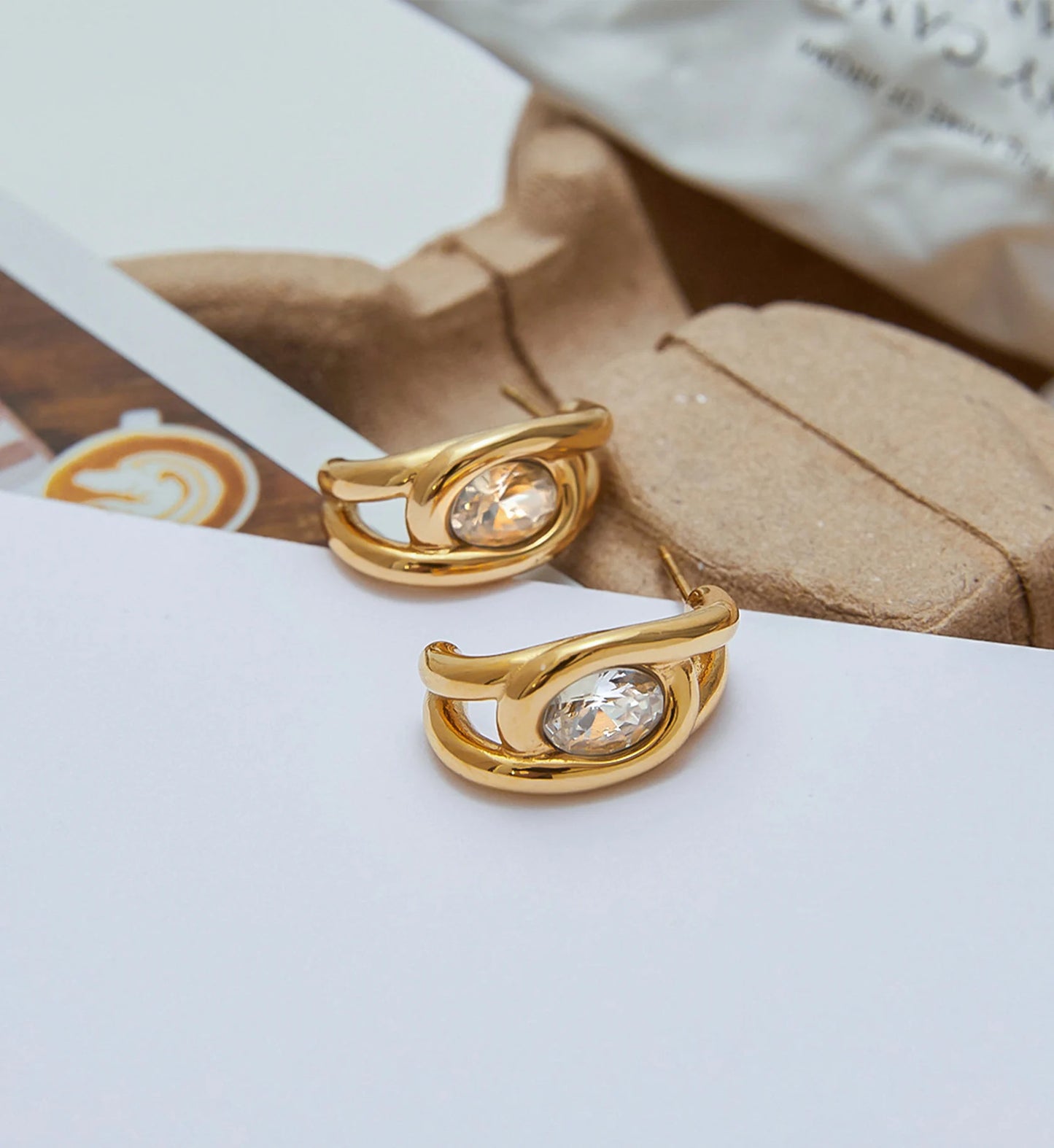 Gold waterproof stainless steel zirconia loop earrings in lifestyle background by Liora Senar