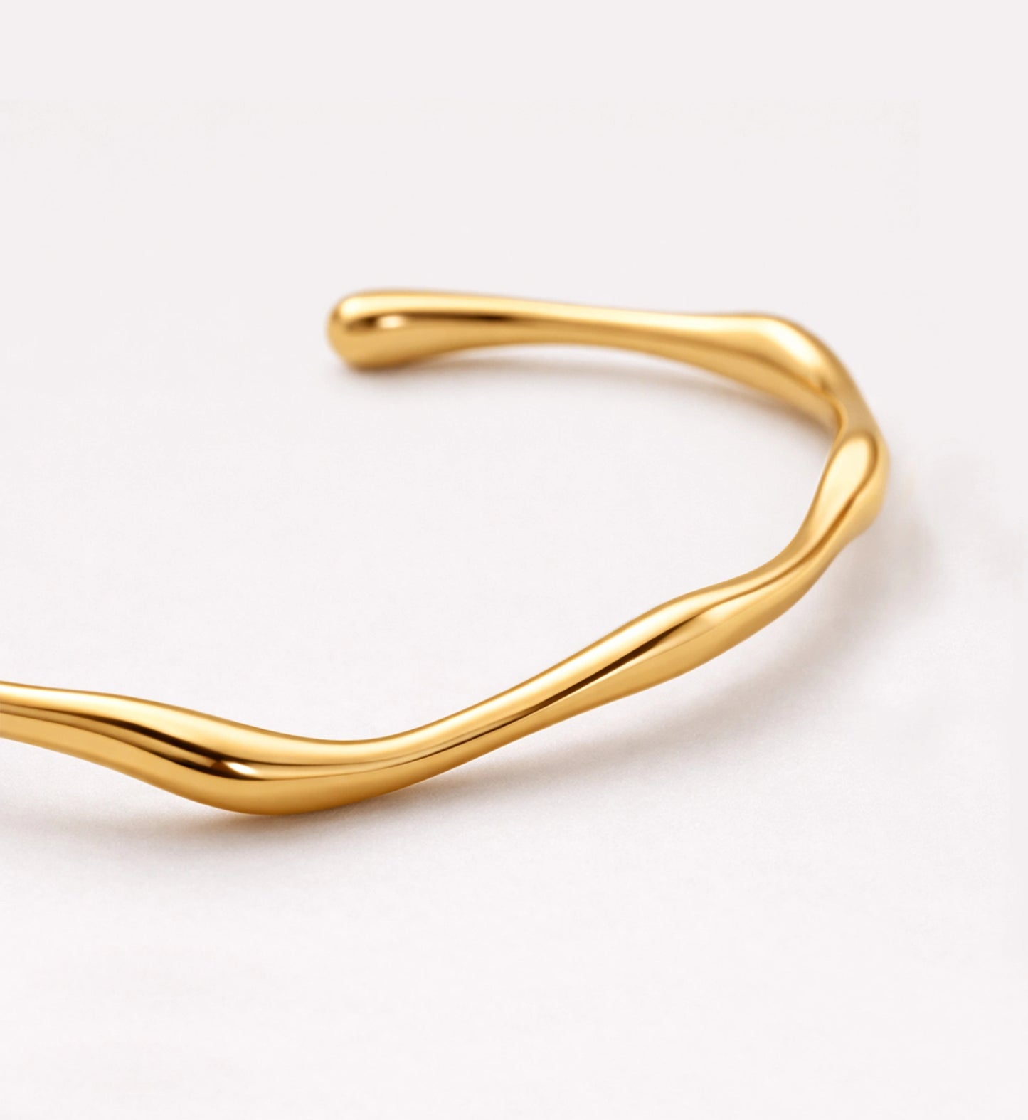 A close-up shot of gold minimalist Aurelian Flow Cuff on white background by Liora Senar