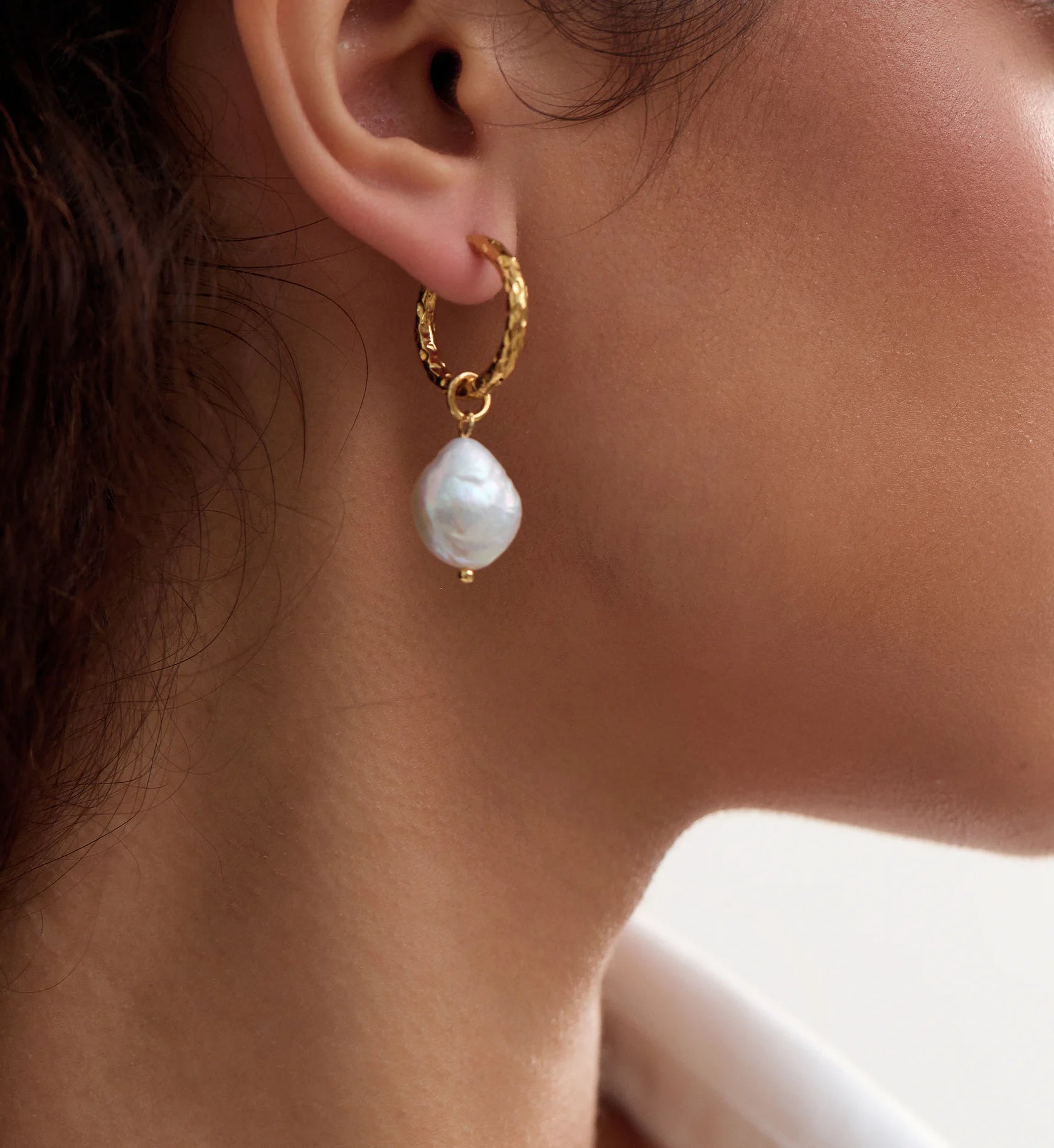 Close-up shot of model wearing natural baroque pearl hoop earrings by Liora Senar