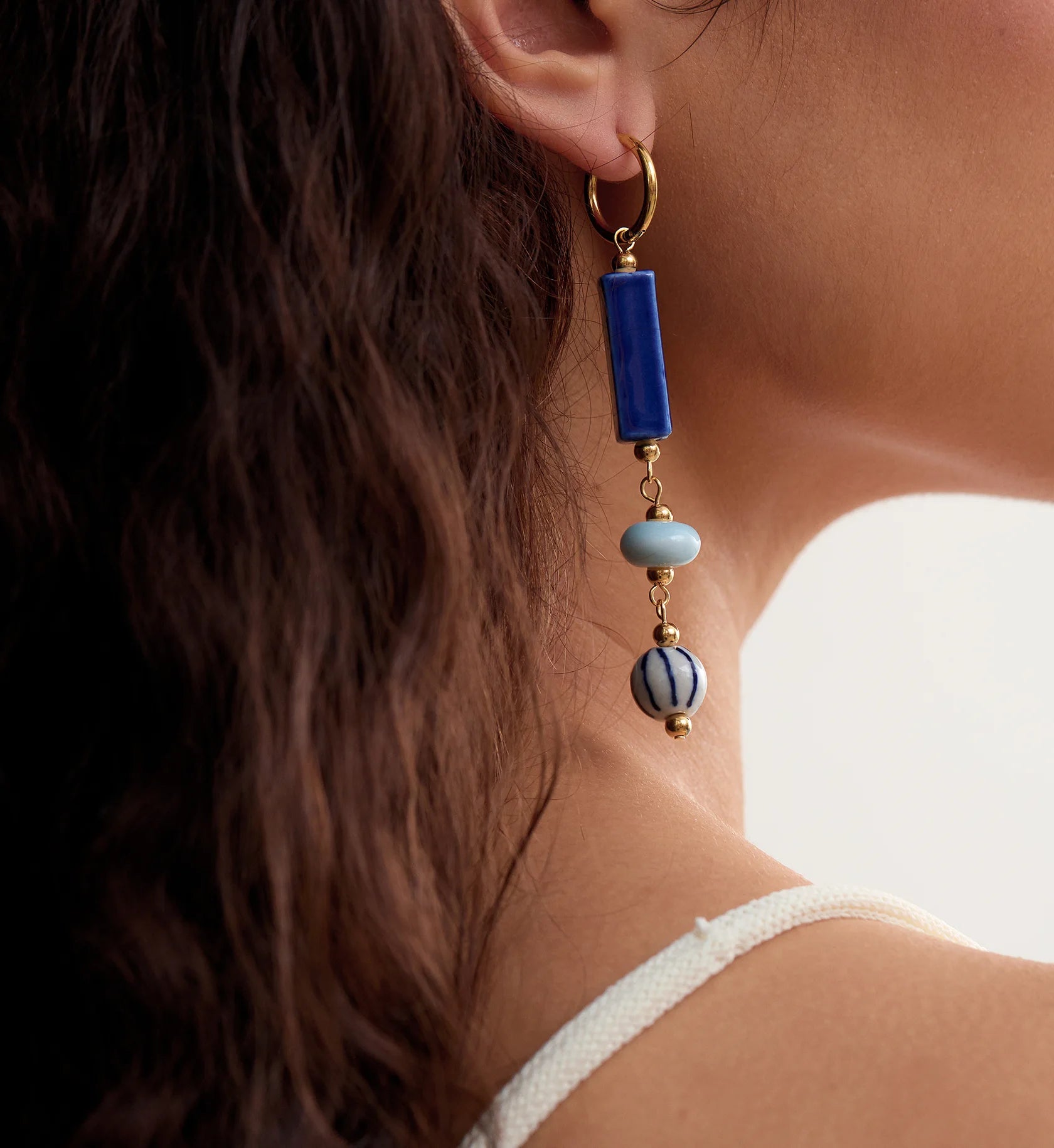 Close-up shot of coastal ceramic dangle earrings on a model by Liora Senar