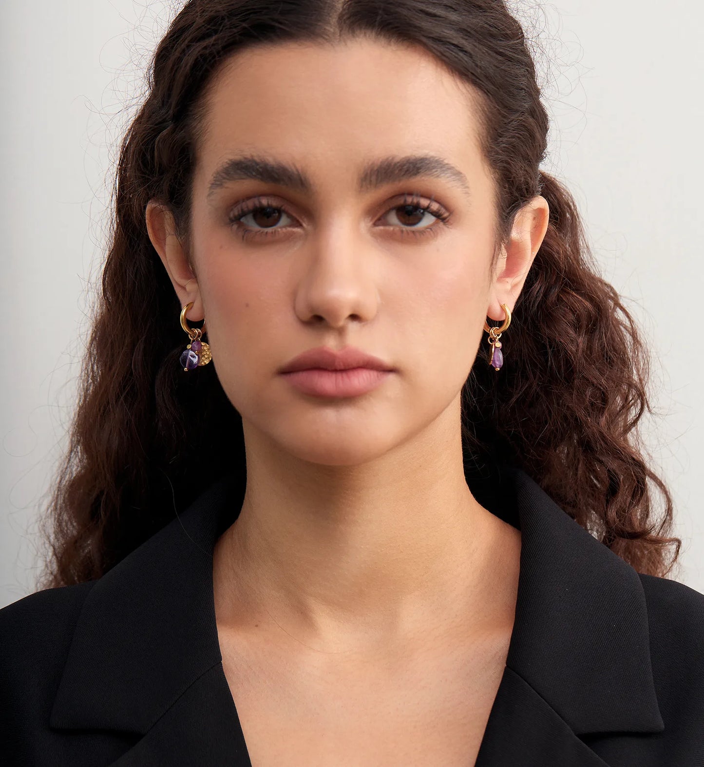 Model wearing a pair of hypoallergenic purple stone hoop earrings by Liora Senar