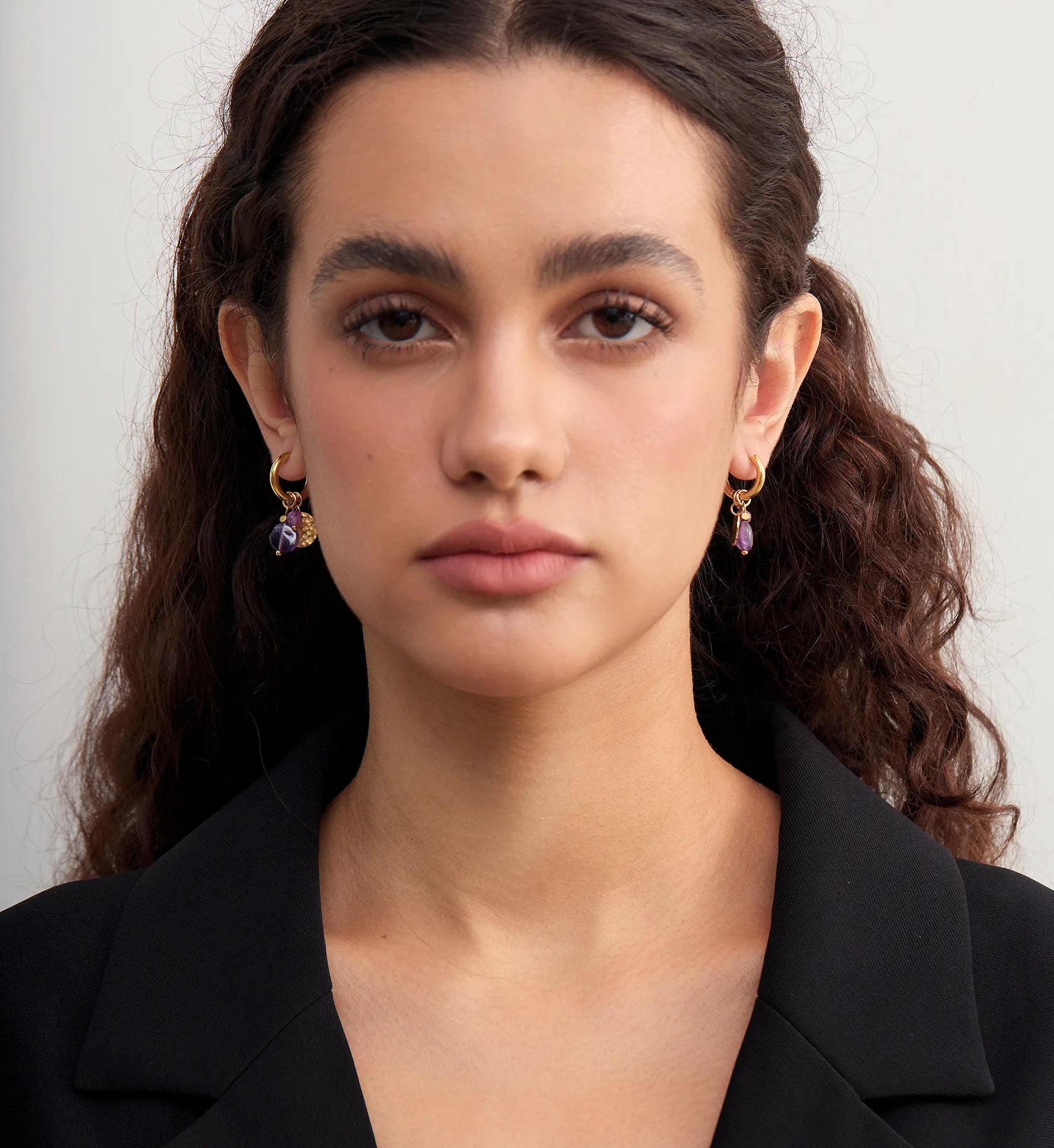 Model wearing a pair of hypoallergenic purple stone hoop earrings by Liora Senar