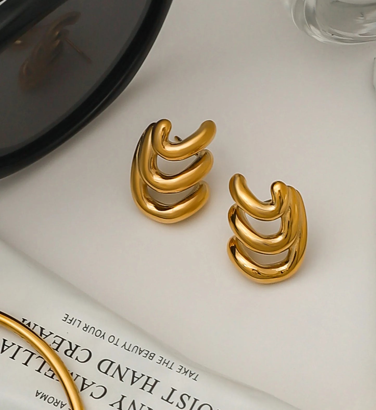 Gold stainless steel ripple curve earrings in a life style background by Liora Senar