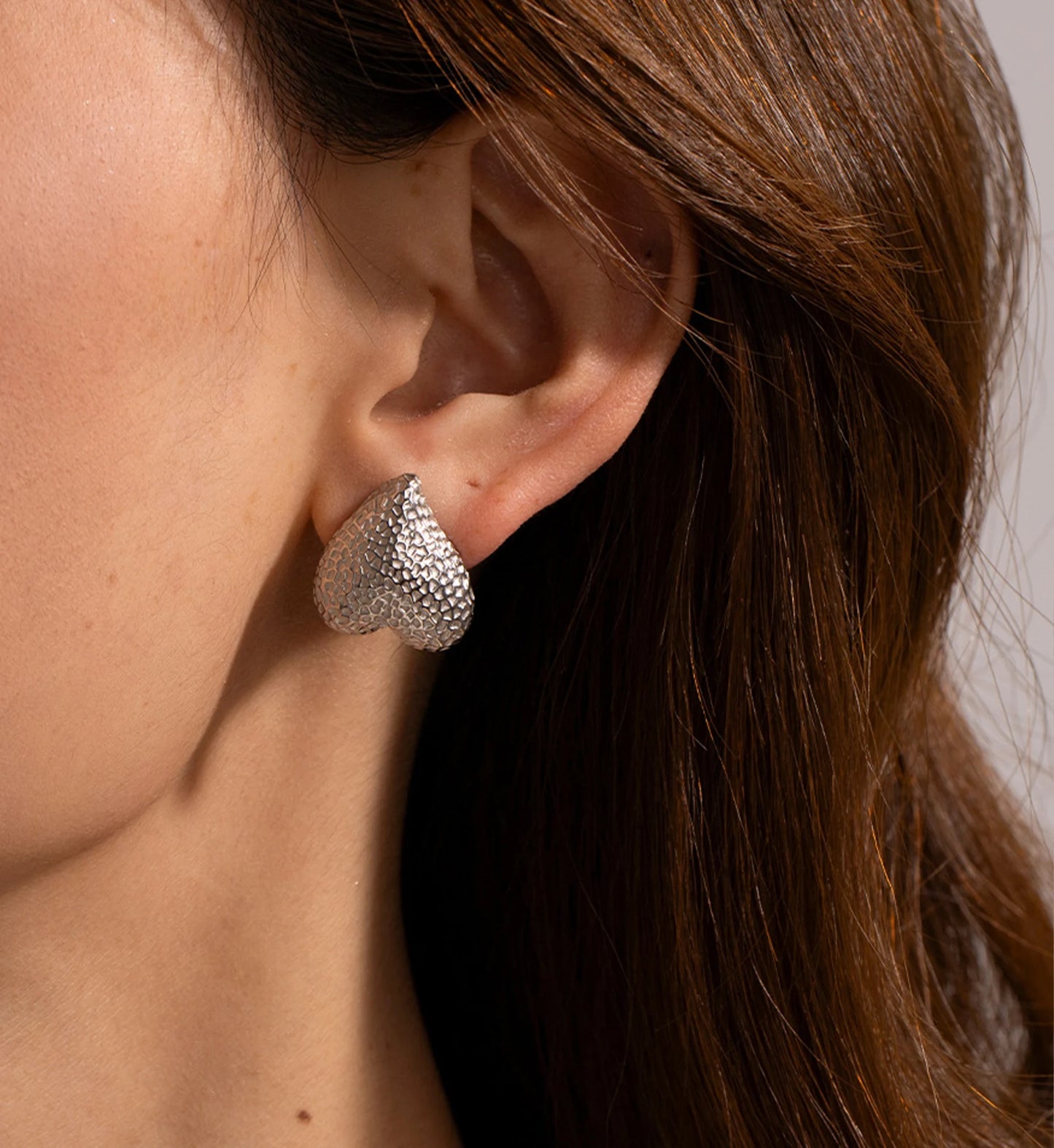 Model wearing silver stainless steel Hammered Metal Heart Earrings by Liora Sennar