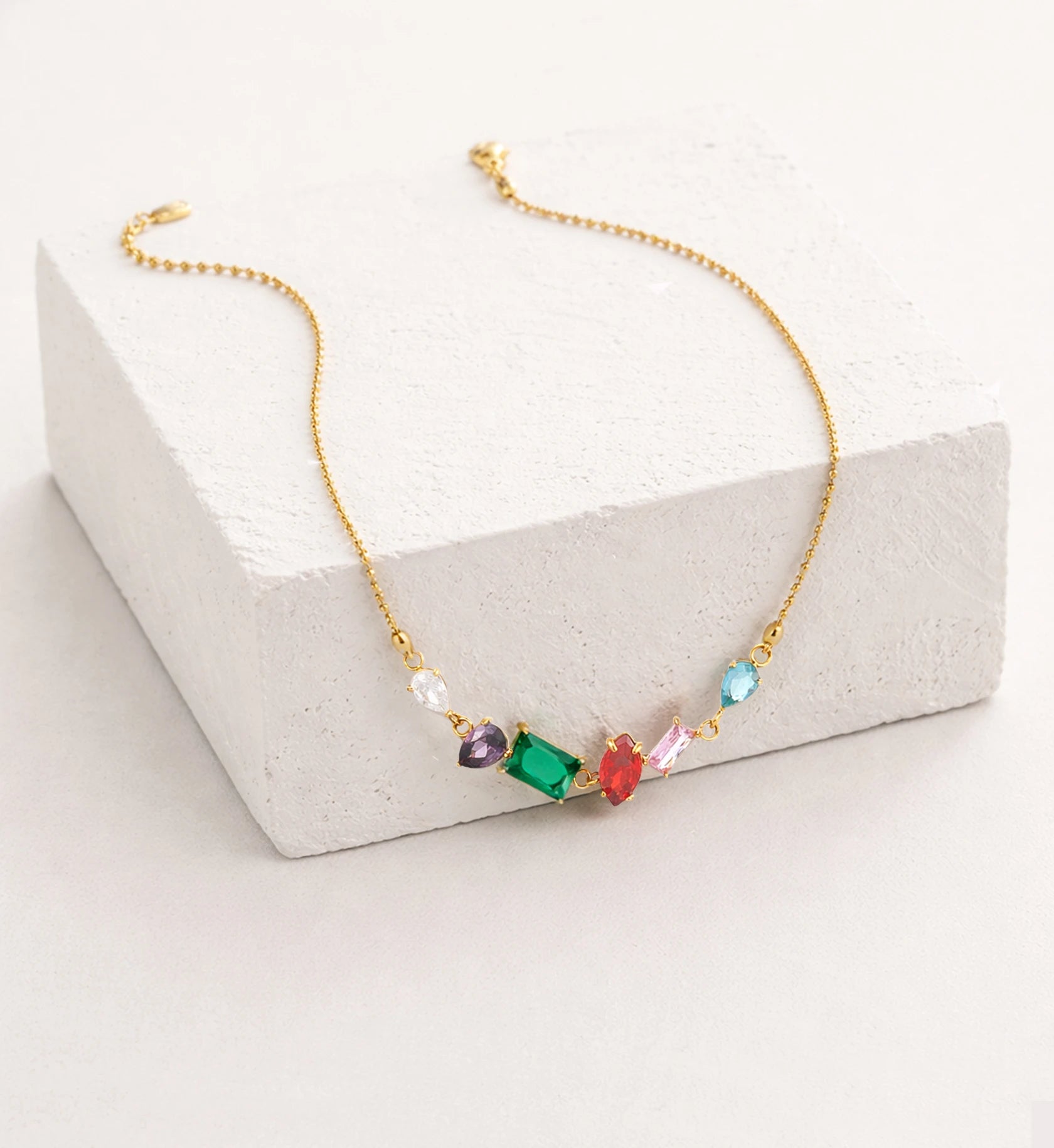 Liora Senar rainbow birthstone gold necklace with colorful gemstones on textured white display block