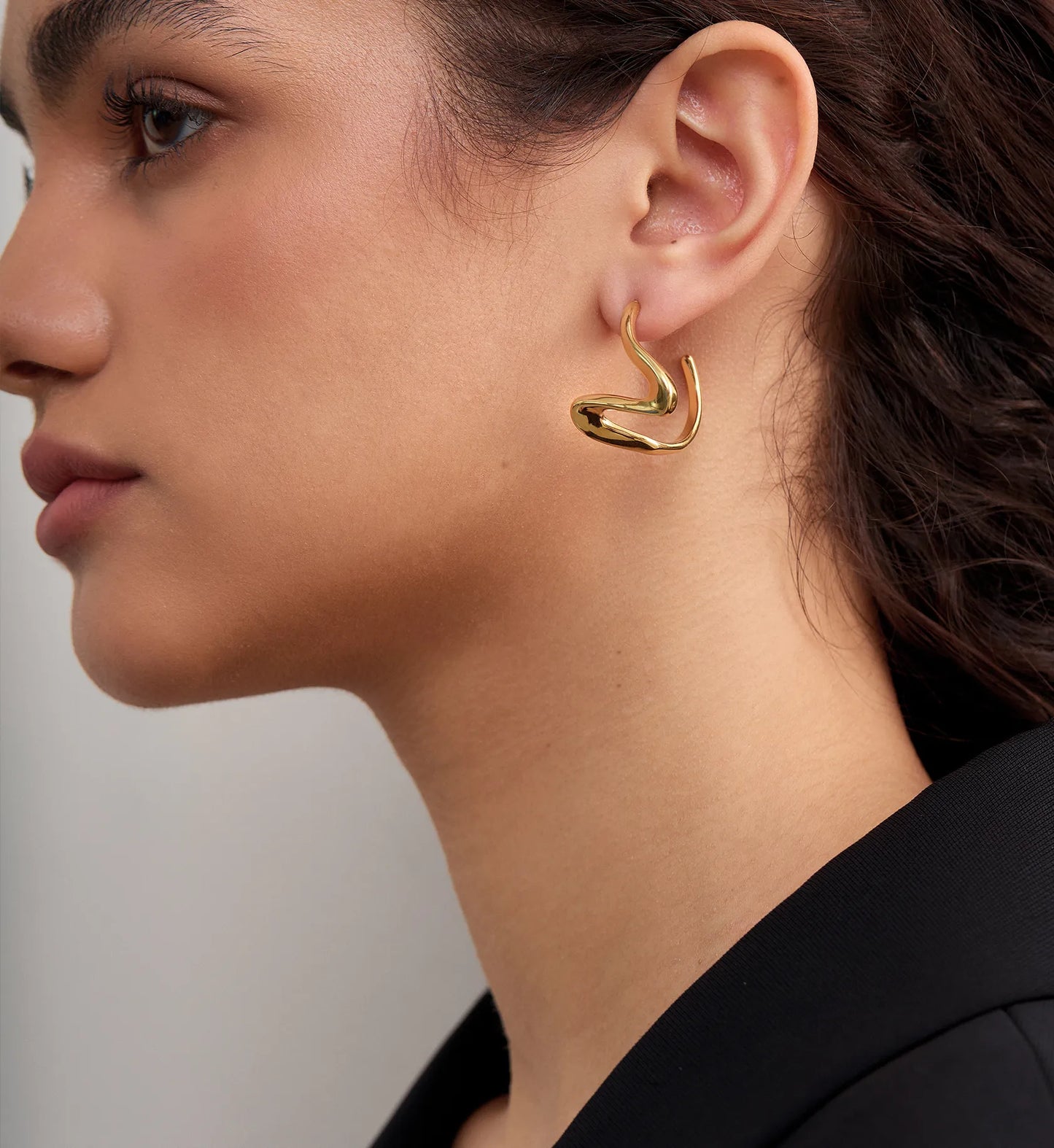 Side image of model wearing minimalist waterproof jewelry sculpted heart hoop earrings by Liora Senar