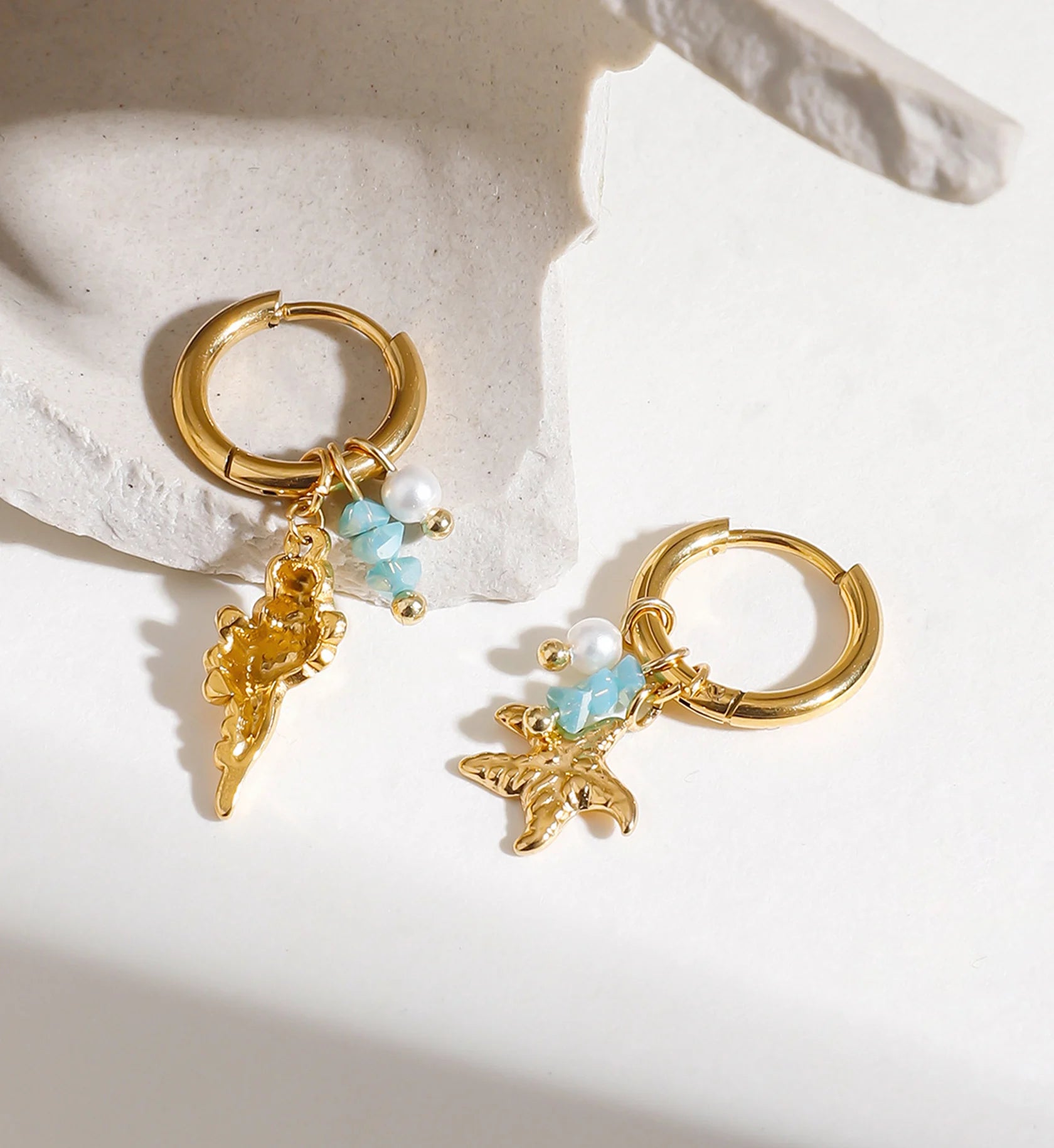 Waterproof stainless steel shell & starfish charms huggie earrings on a stone by Liora Senar
